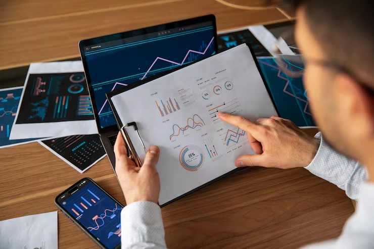 Professional analyzing data reports and charts on tablet with laptop displaying analytics dashboards and metrics